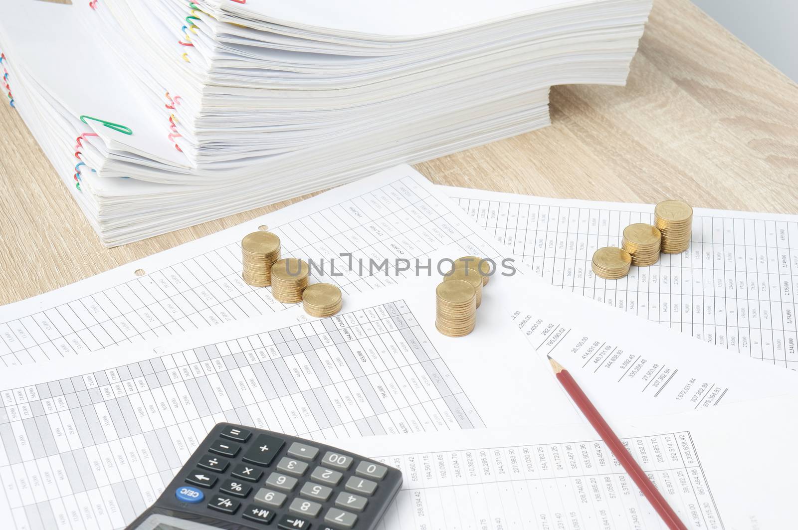 Pencil and step pile of gold coins on finance account have overload paperwork of report as background on wooden table. Stack document of account as work hard. Business and finance concept successful.