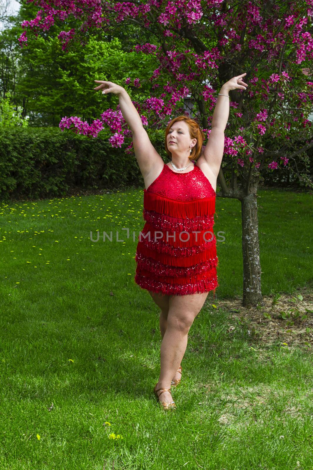 forty something brunette woman wearing a sparkling red dress, dancing under a tree