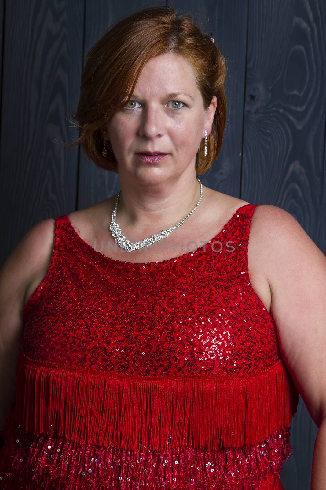 forty something brunette woman wearing a red sparkling dress in front of blue wood panel