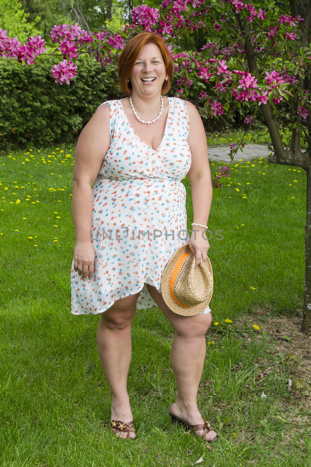 forty something woman under a cherry tree holding a straw hat