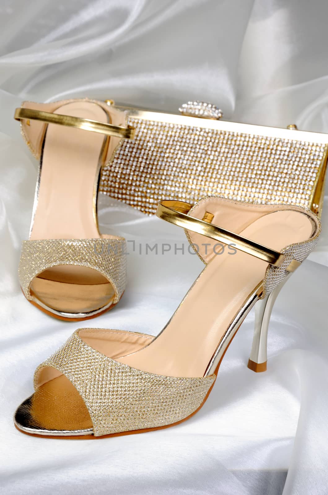 A pair of gold sandals with a high heel, with a golden clutch on the table