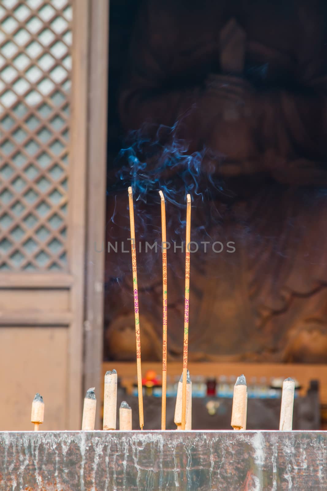 Burning incense at a stone alter in front of a temple housing a giant wooden sculpture of Buddha.