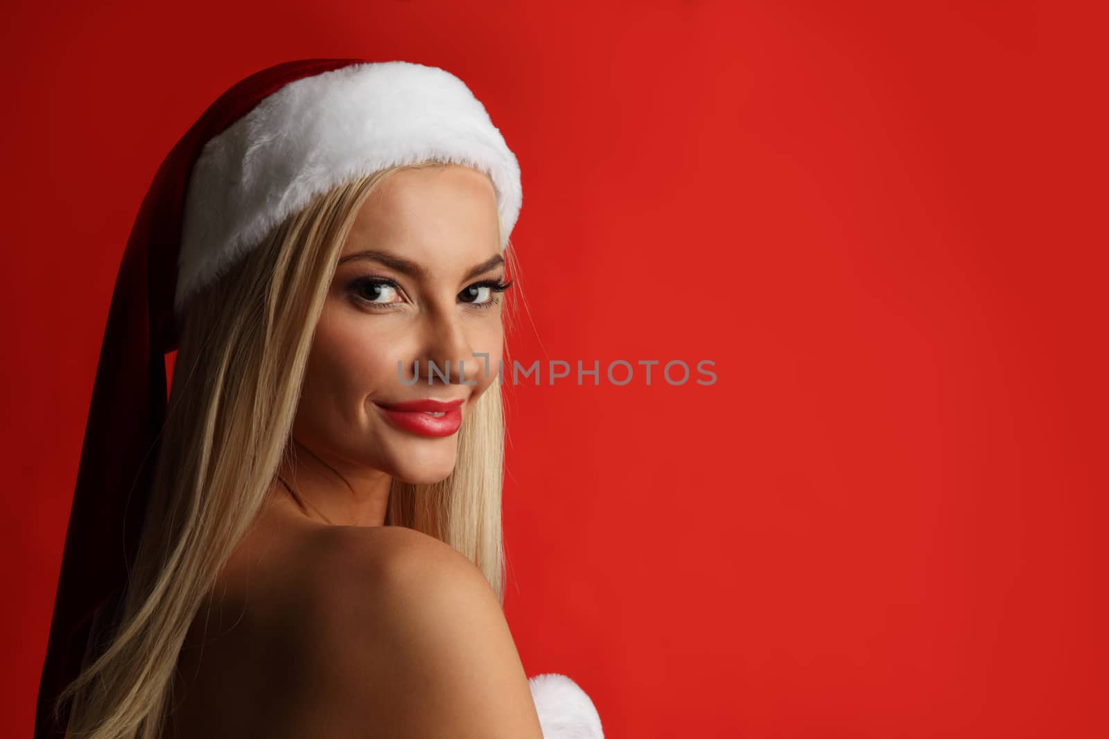 Portrait of a happy attractive young woman posing in red santa claus costume on red background with copy space