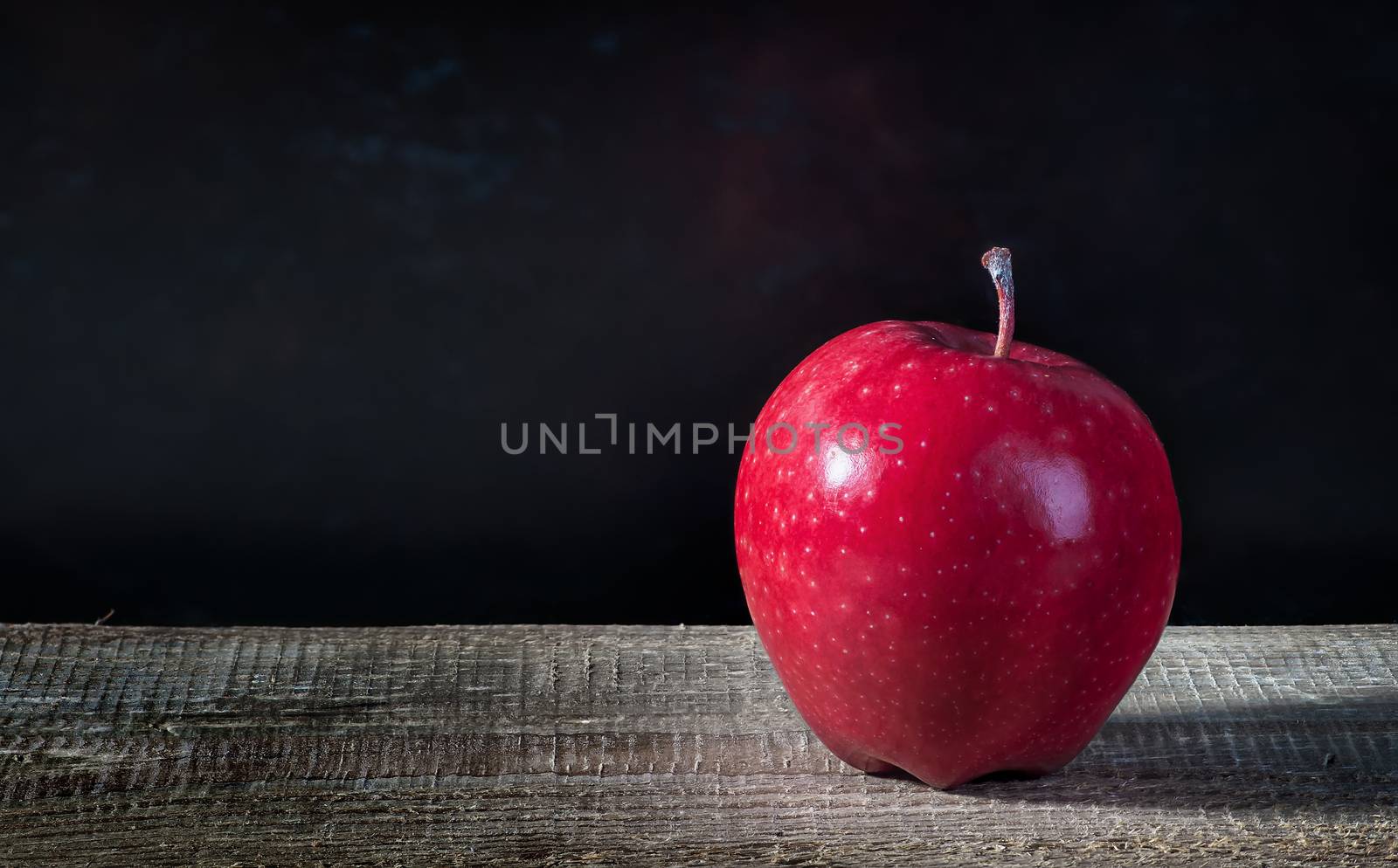 Single apple on a wooden table. Blurred dark background.