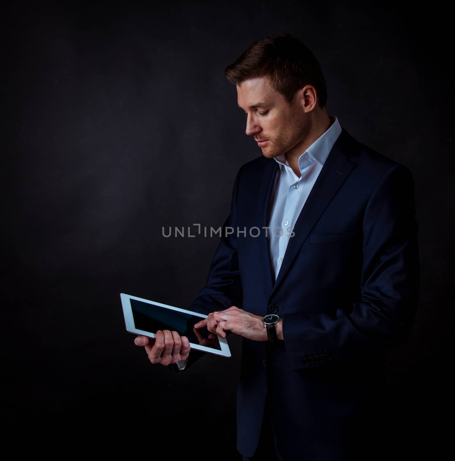 Young handsome businessman using digital tablet, studio shot on dark background