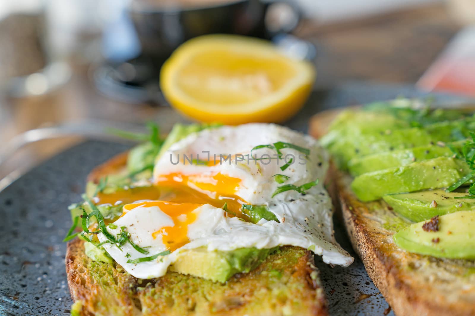 Breakfast served and started poached egg with yoke running onto sliced avocado and toast in selective focus.