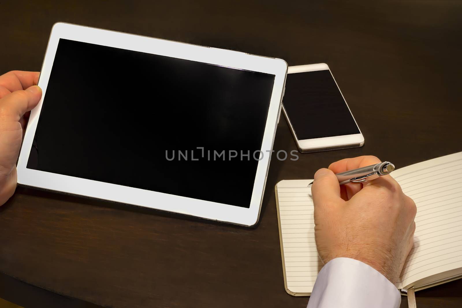 Work place - a businessman writes information from a tablet to the notebook