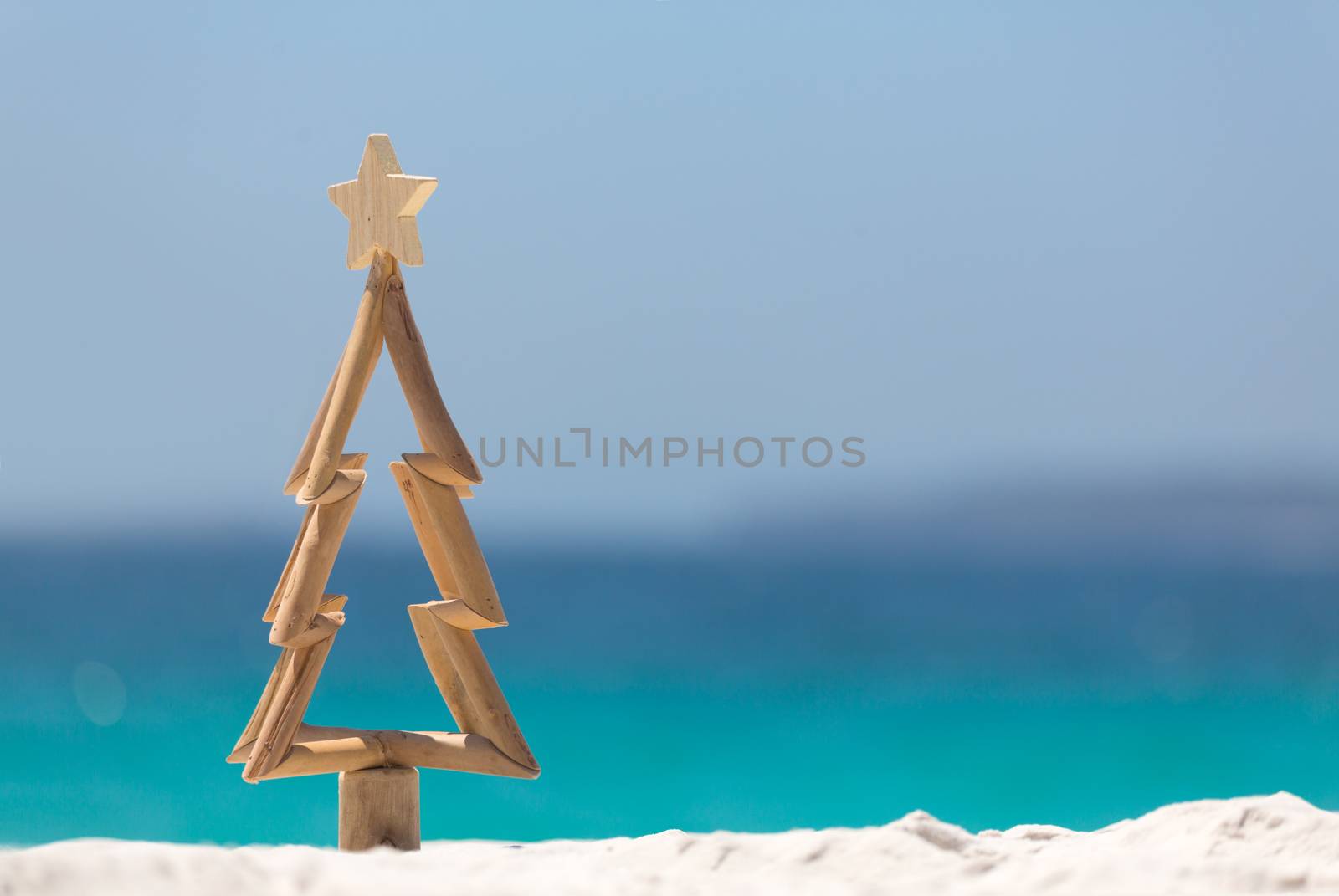 Timber Christmas tree with star sits in pristine white sand with idyllic beach background.  A summer Christmas.  