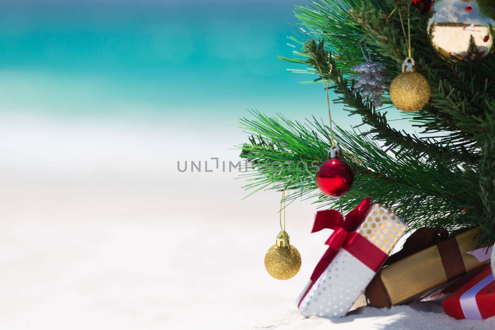 Christmas time spent at the beach in summer. A christmas tree surrounded by presents on a beautiful sandy beach.  Shallow dof with space for copy