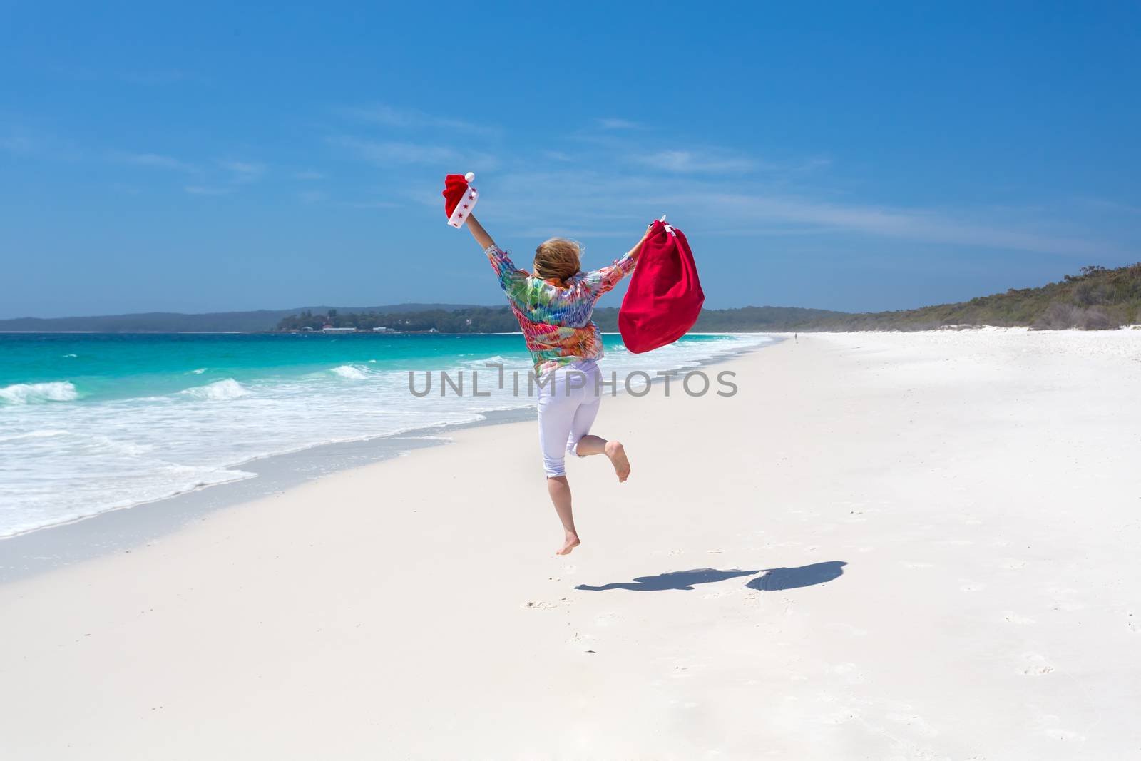 Celebrating Christmas in Australia, hot sunny days and lazy days down at the beach.  A woman jumps for joy on a beautiful stretch of white sandy beach.  Christmas celebration, Christmas vacation, space for copy