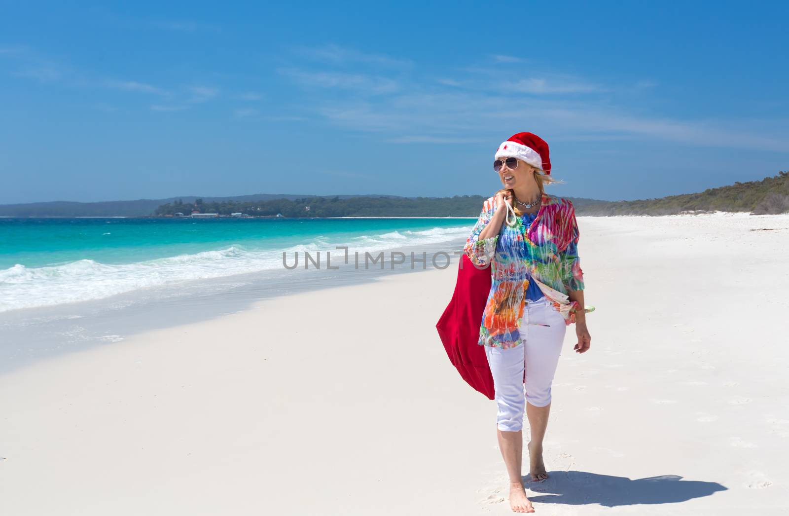 Hot summer days Christmas down on the beach or summer vacation southern hemisphere.  A casually dressed female strolling along the beach wearing a red santa hat.