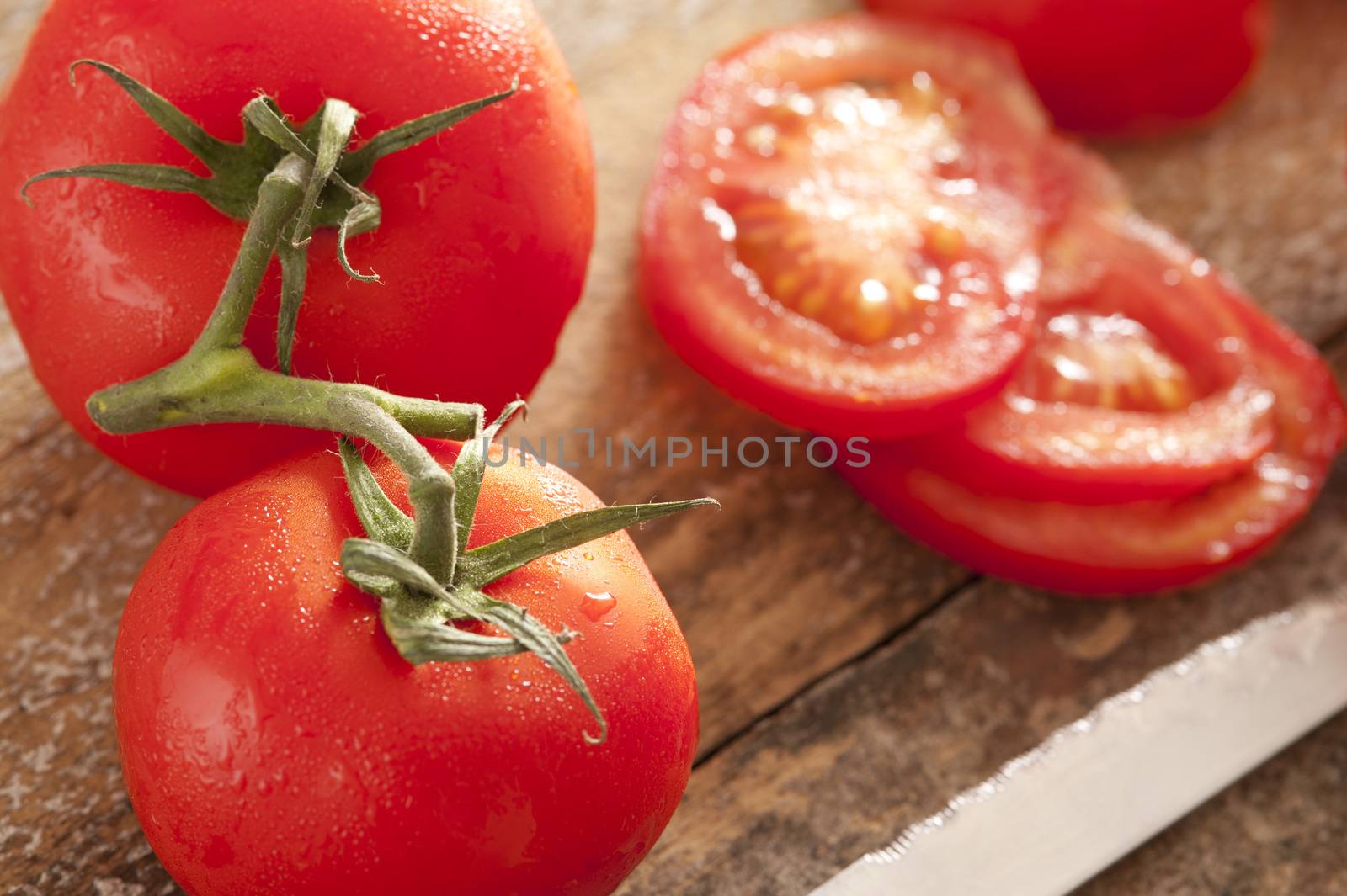 Fresh washed tomatoes with droplets of water on the vine and sliced ready for inclusion in a healthy summer salad on a wooden board with knife
