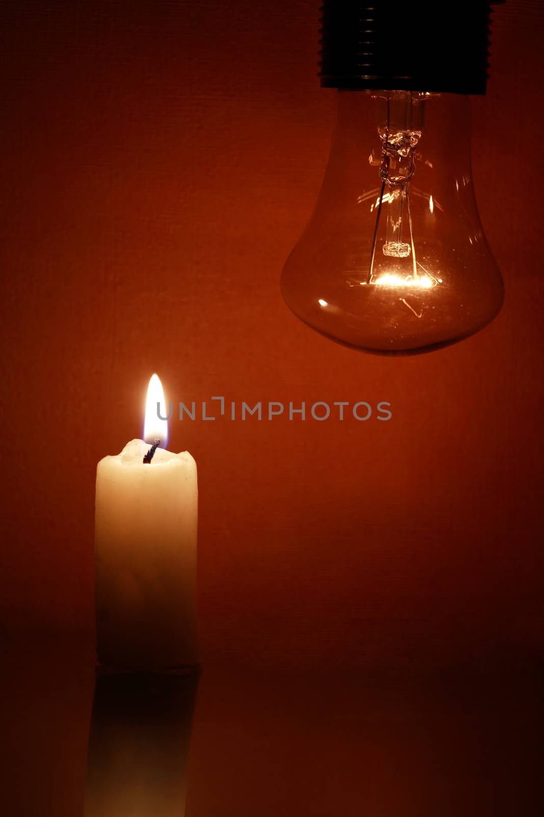 Closeup of glowing light bulb near lighting candle