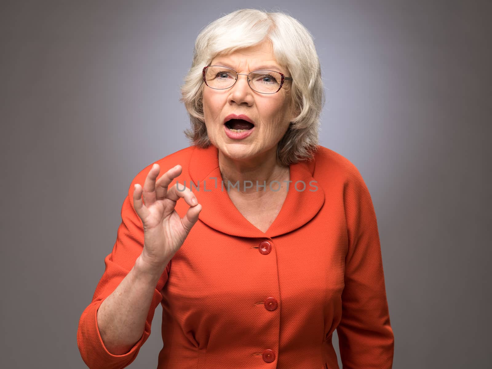 Smiling senior lady showing ok sign on gray background