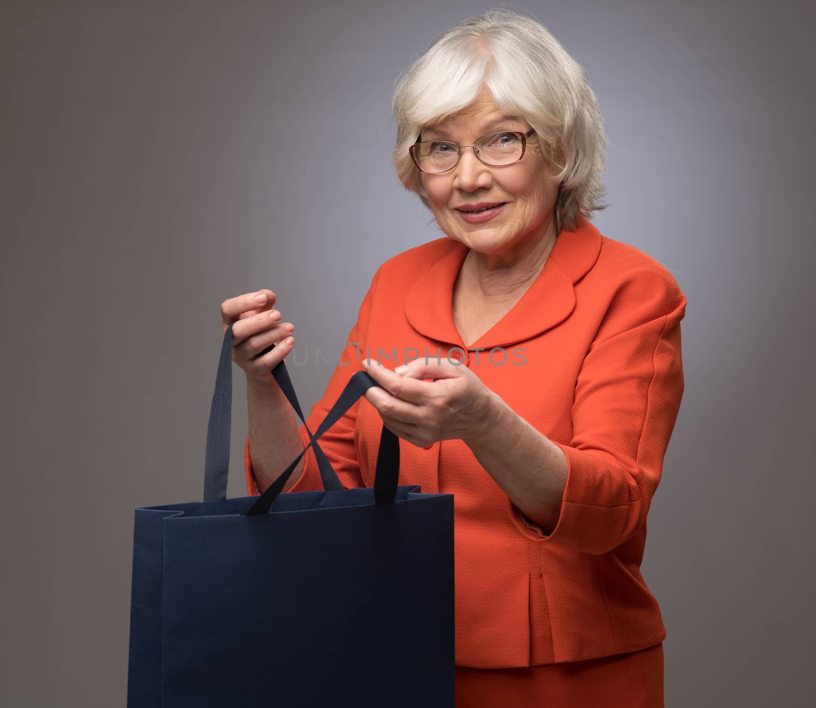 Smiling senior lady with shopping bag on gray background with copy space