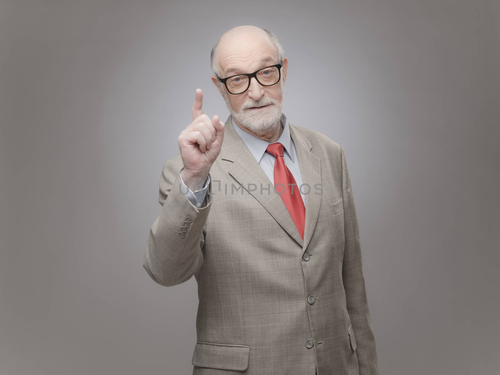 Senior man points finger up on gray background with copy space