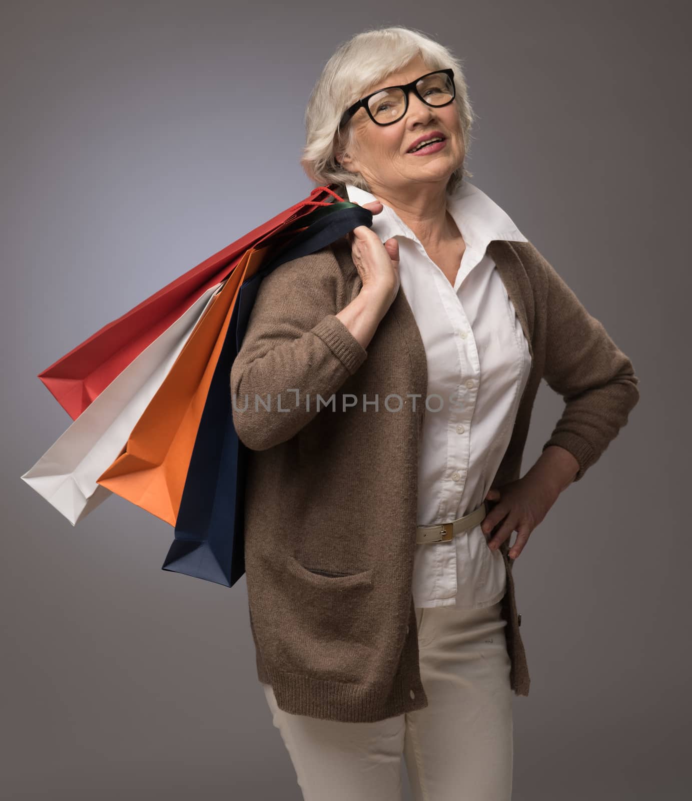 Studio portrait of happy senior woman with shopping bags