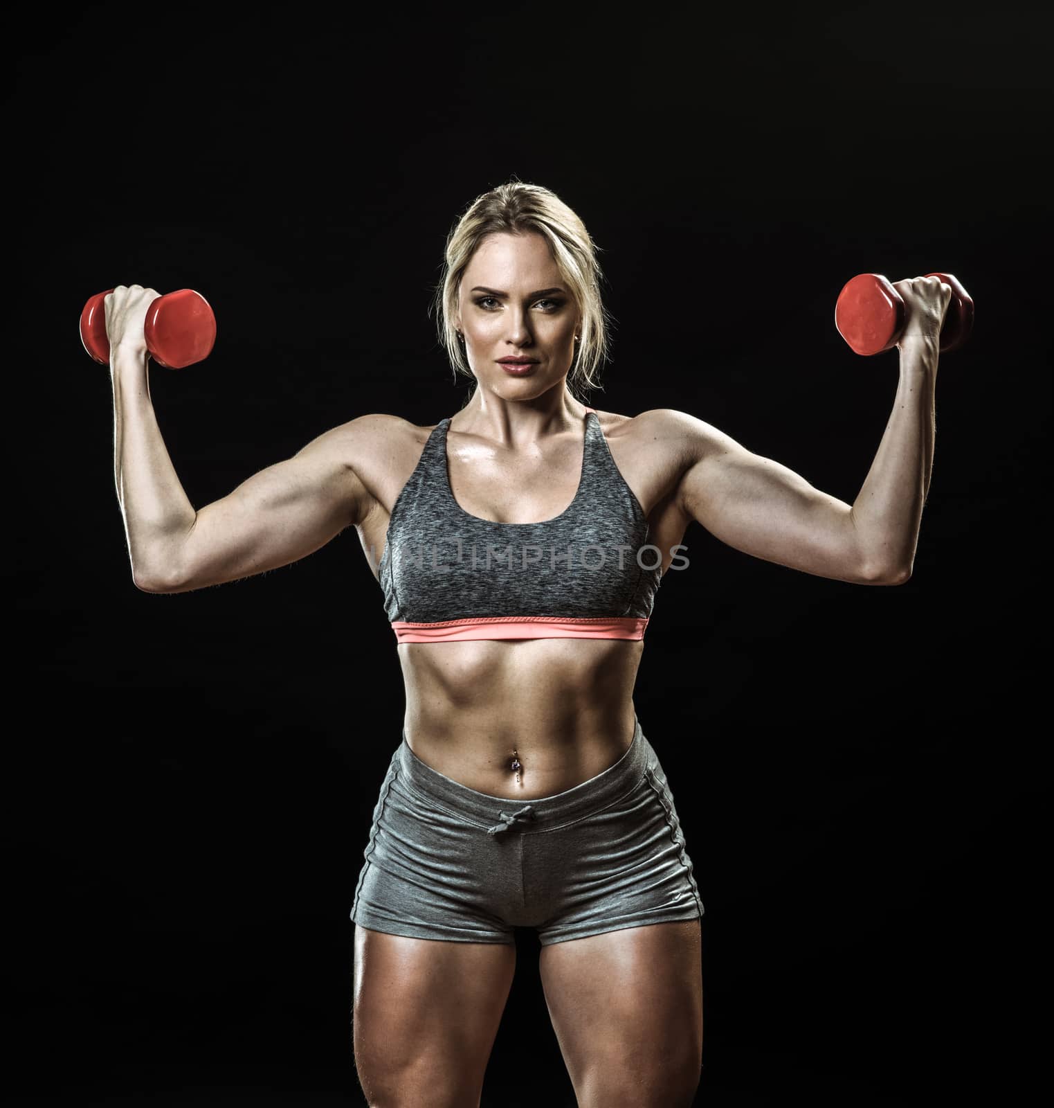 Beautiful muscular woman lifting dumbbells isolated on black background