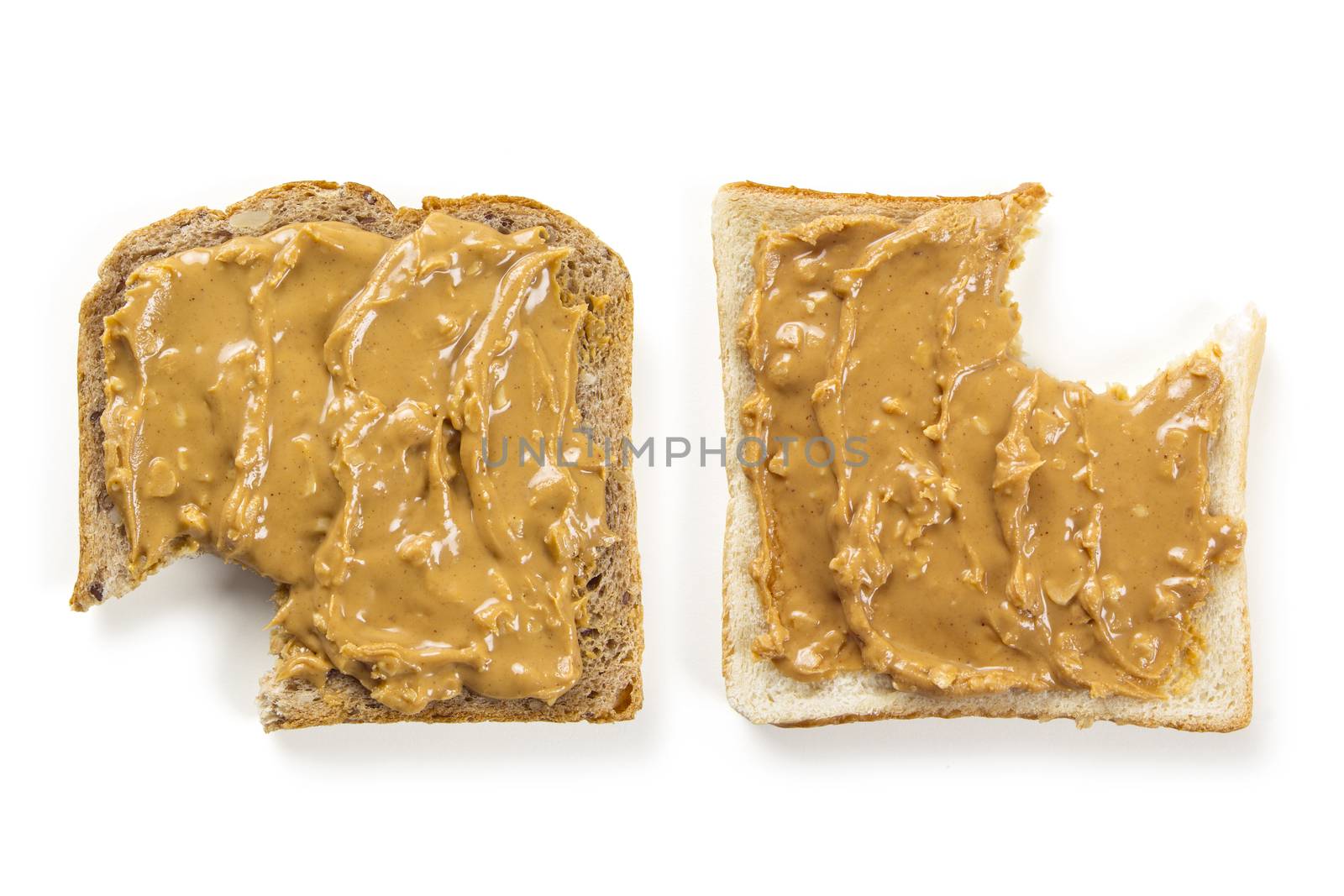 Photo of two slices of white and whole wheat bread covered in peanut butter, isolated on white, with bites.