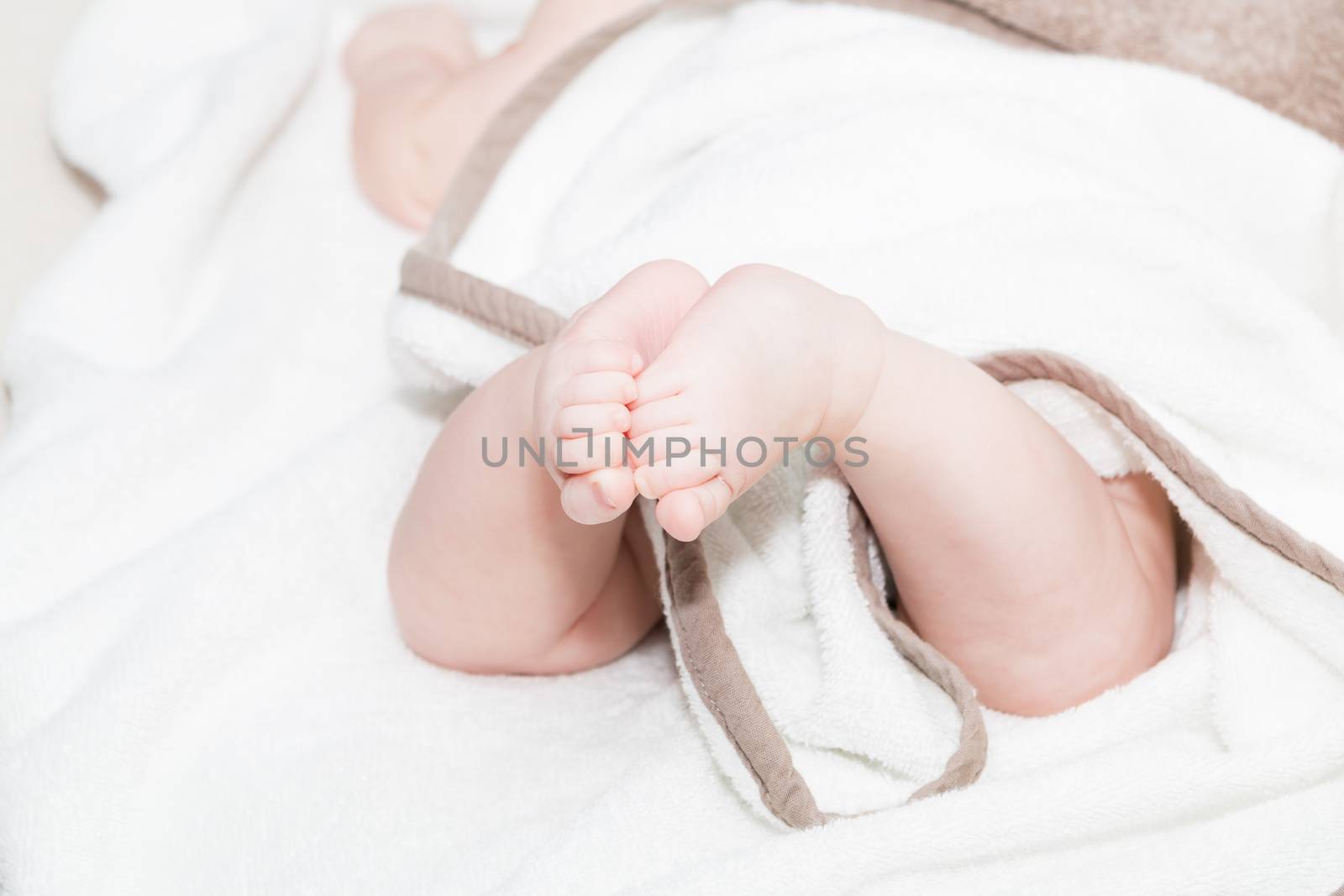 Baby feet under white blanket cover. Close up picture of new born baby feet on a white sheet.