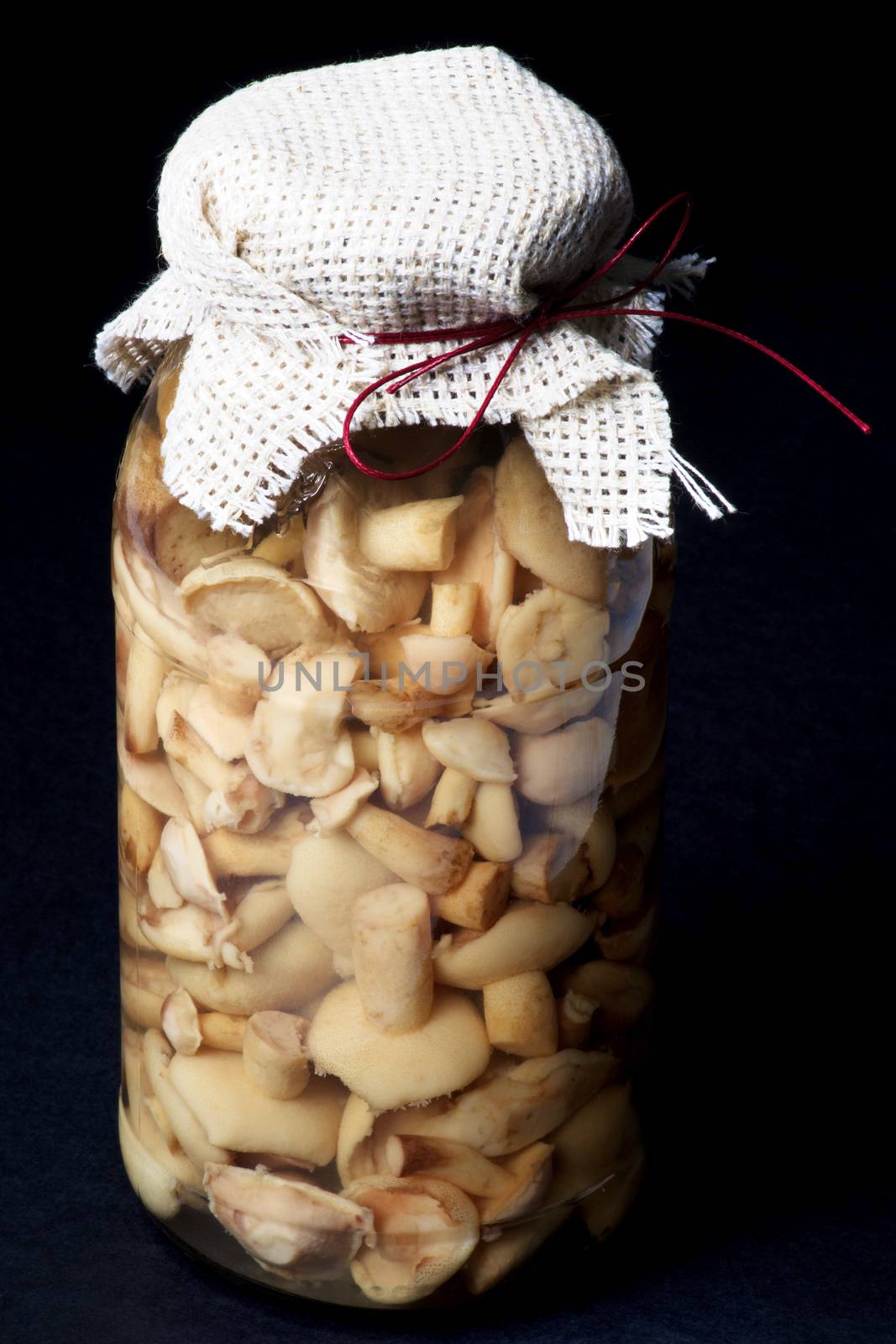 Marinated Peppery Milkcap in Glass Jar with Sack and Bow isolated on Black background