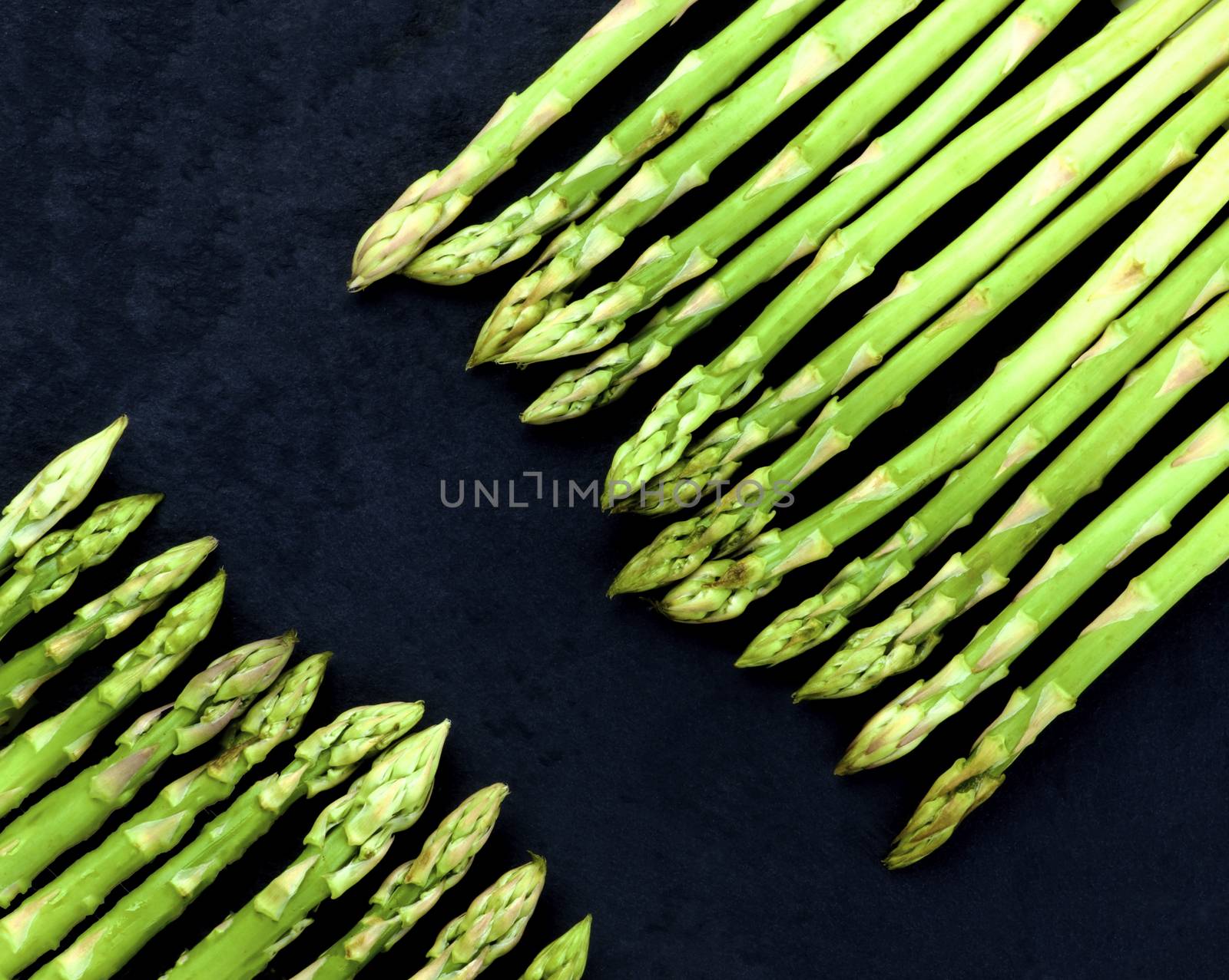 Borders of Fresh Asparagus Sprouts closeup on Black Slate background