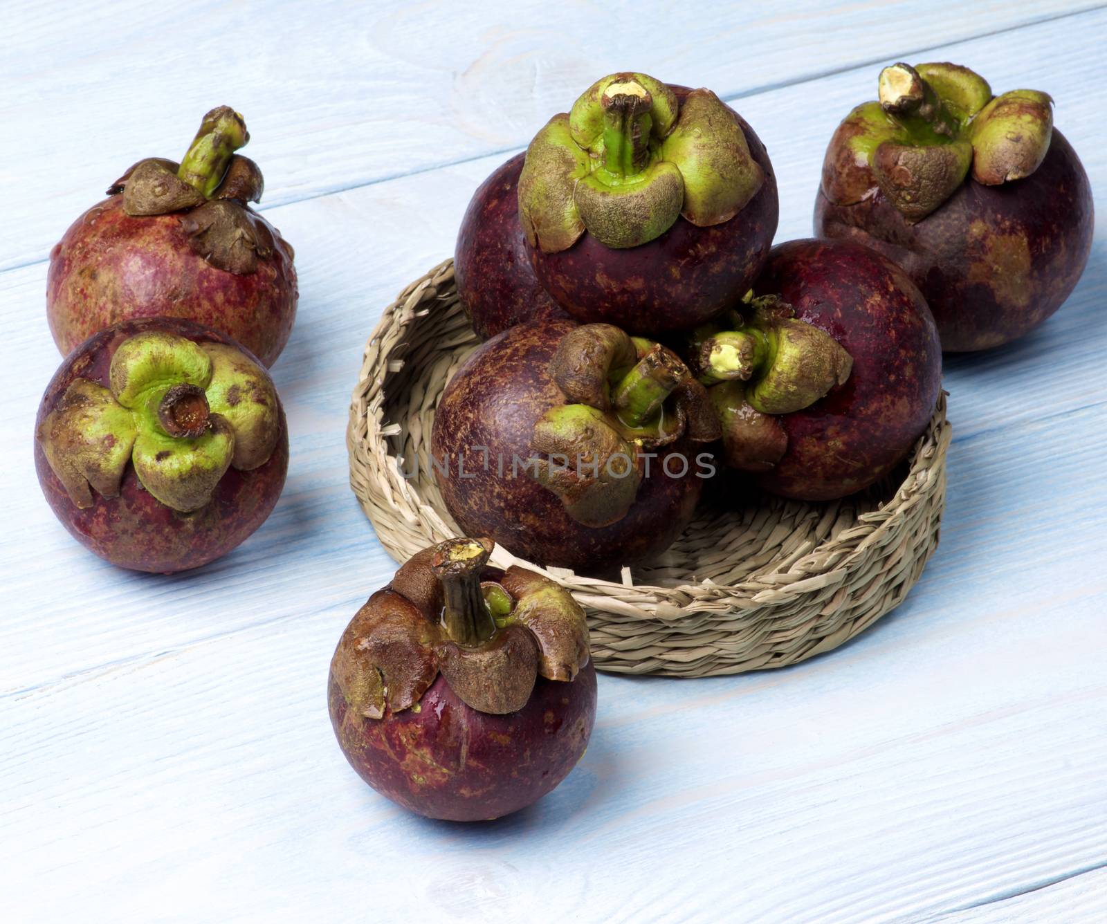 Stack of Fresh Ripe Mangosteen in Wicker Bowl closeup on Light Blue Wooden background