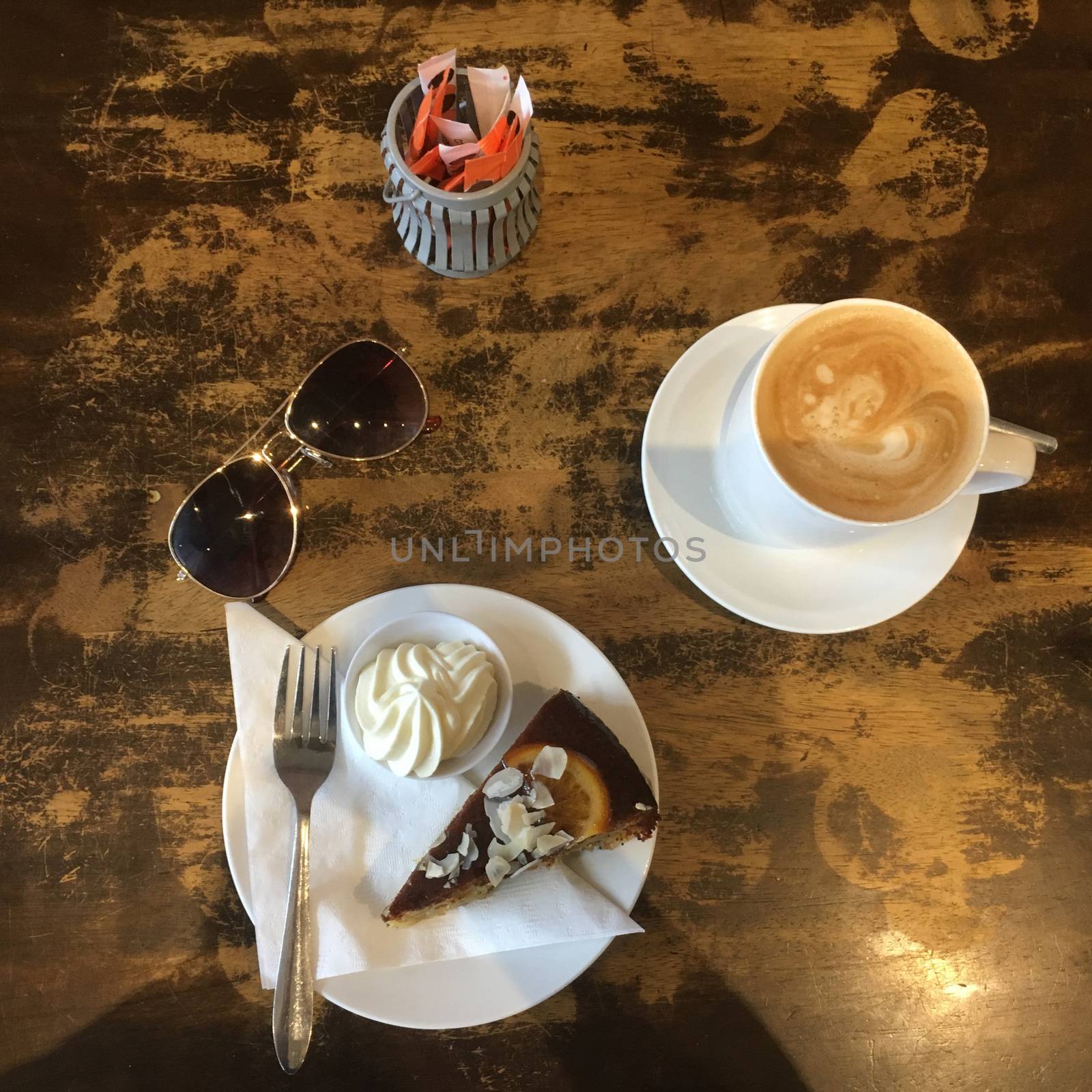 Before Shot.   Top View of a slice of gluten free orange and poppyseed cake with a side of cream and a coffee in a mug in a rustic cafe