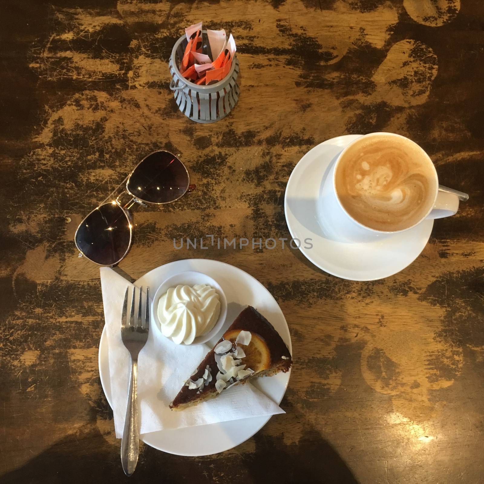 Before Shot.   Top View of a slice of gluten free orange and poppyseed cake with a side of cream and a coffee in a mug in a rustic cafe