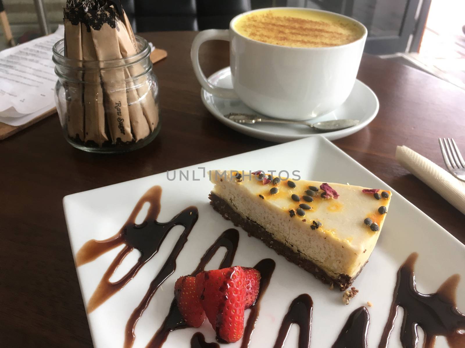 AIP Autoimmune Paleo or healthy organic eating choices.  Slice of cashew milk cheesecake on a plate and behind a golden tumeric latte.  On a table in a wellness organic cafe. Gluten free dairy free food