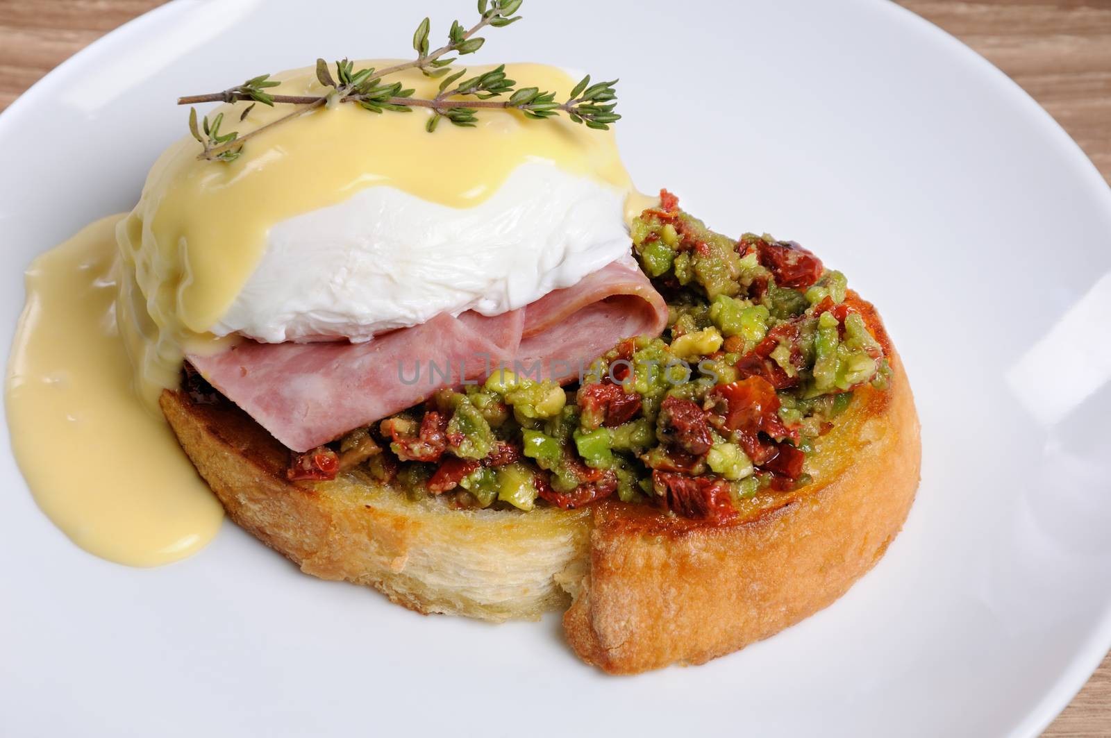 Toasted baguette slice with guacamole, ham and eggs Benedict under Dutch sauce