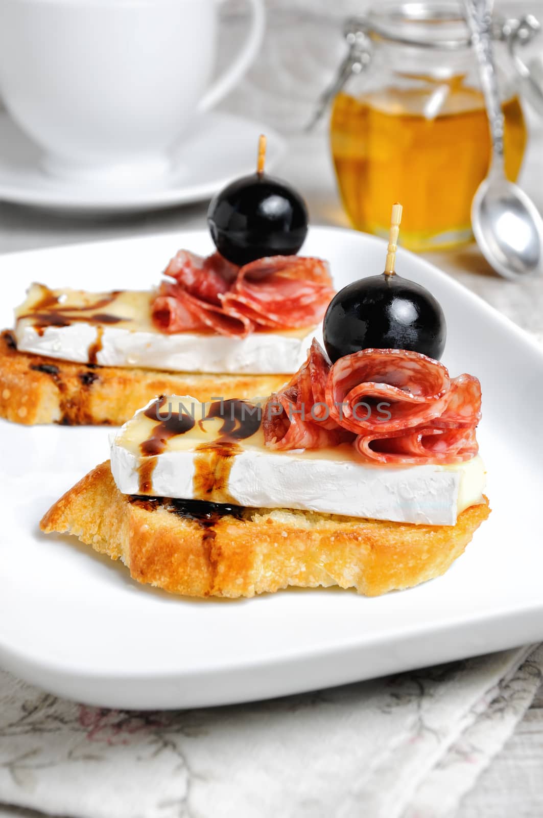 Snack from a toasted slice of baguette with soft under a noble white mold Cheese Brie, salami, a berry of grapes with honey