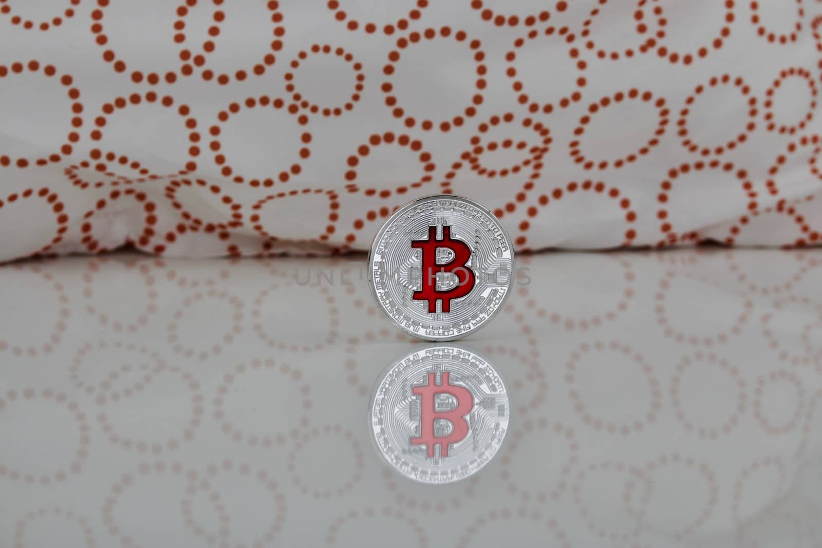 Cryptocurrency physical silver bitcoin coin with red sign on the white and orange scene.