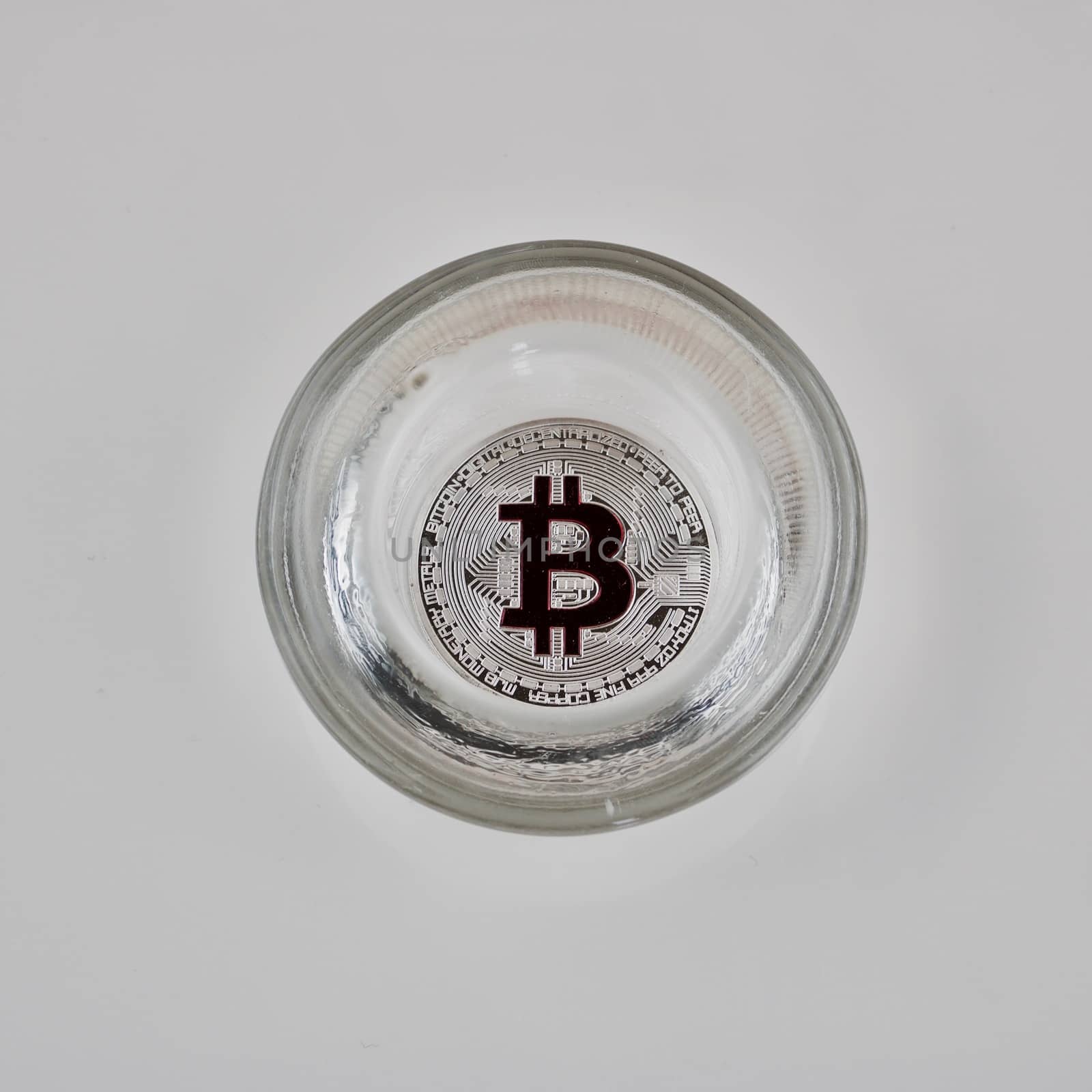 Digital currency physical silver bitcoin coin in glass jar on the white background.