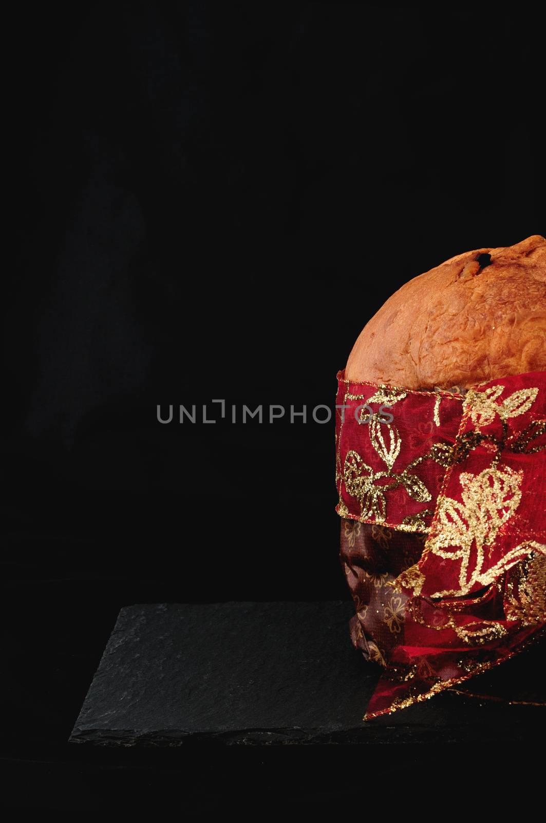 christmas essence, panettone with red ribbon on black background, vertical. Panettone is a typical Christmas cake in Italy