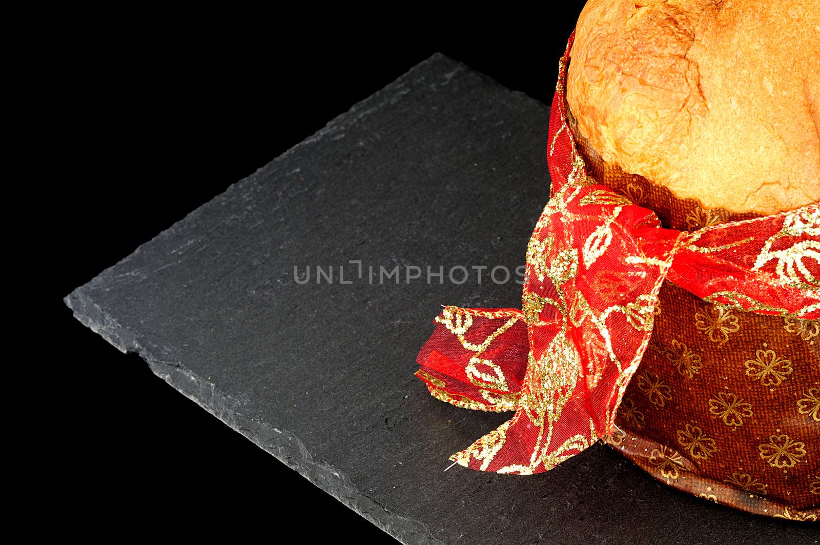 Christmas background, close up on panettone with red ribbon, slate dish on black background. copy space 