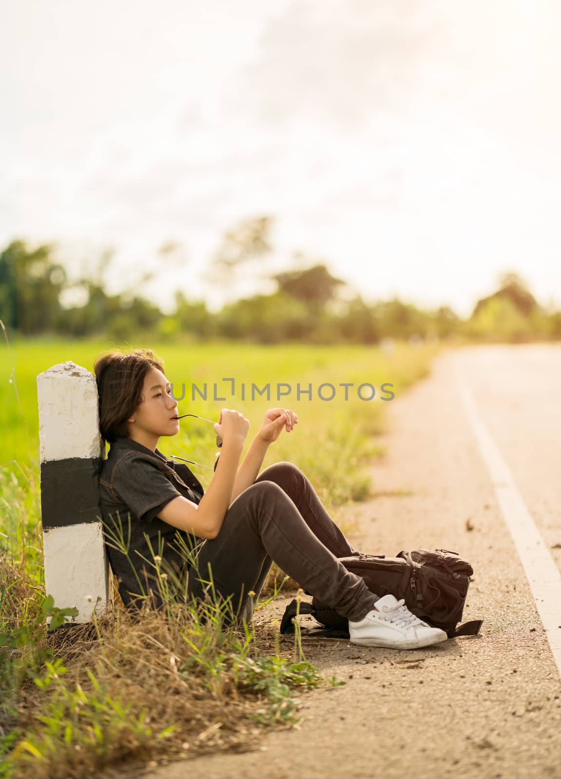 Woman sit with backpack hitchhiking along a road in countryside by stoonn