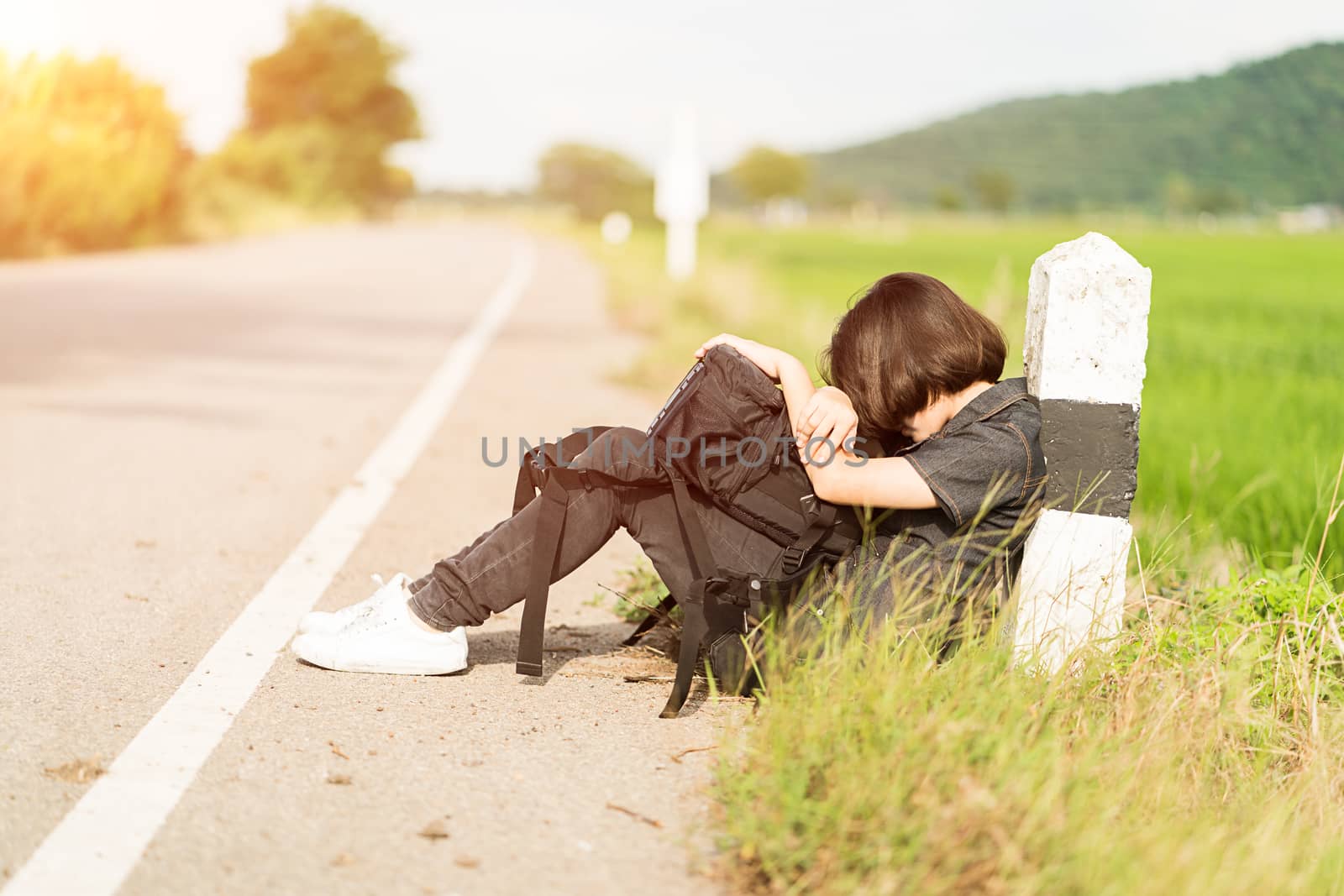 Young asian woman short hair and wearing sunglasses sit with backpack hitchhiking along a road wait for help in countryside Thailand