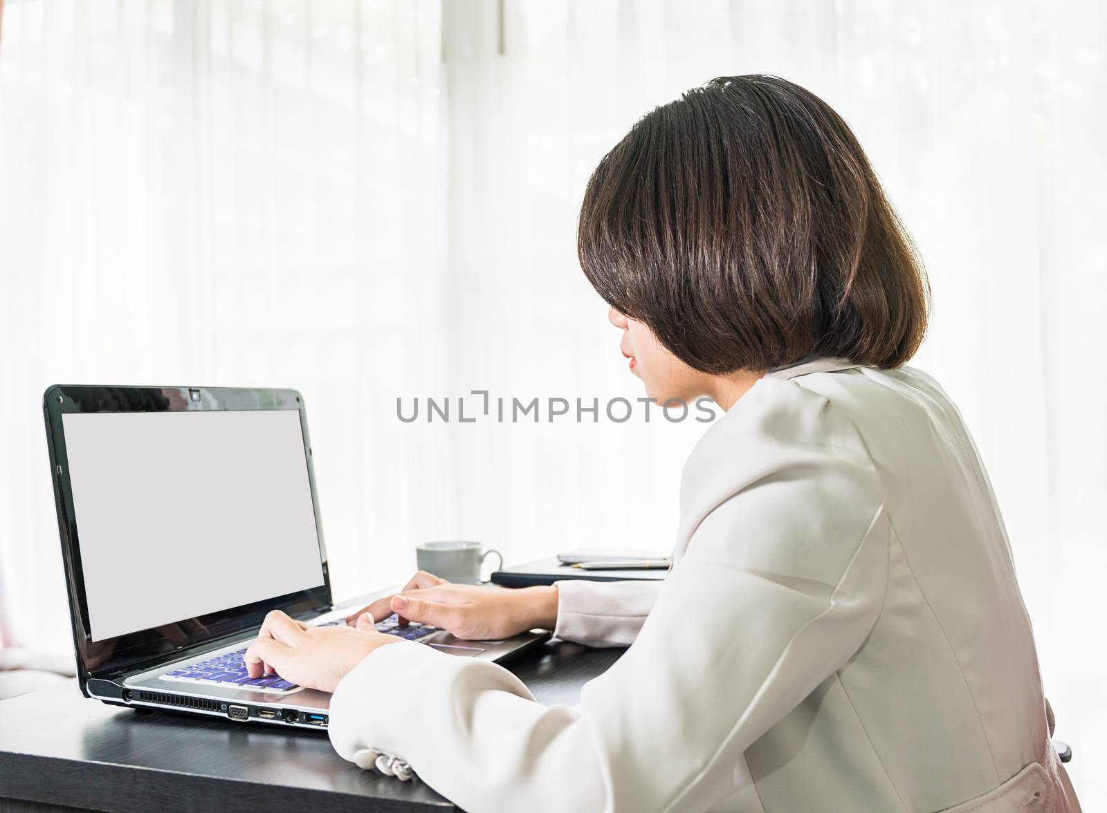 Young asian woman short hair in smart casual wear working on laptop while sitting near window in home office