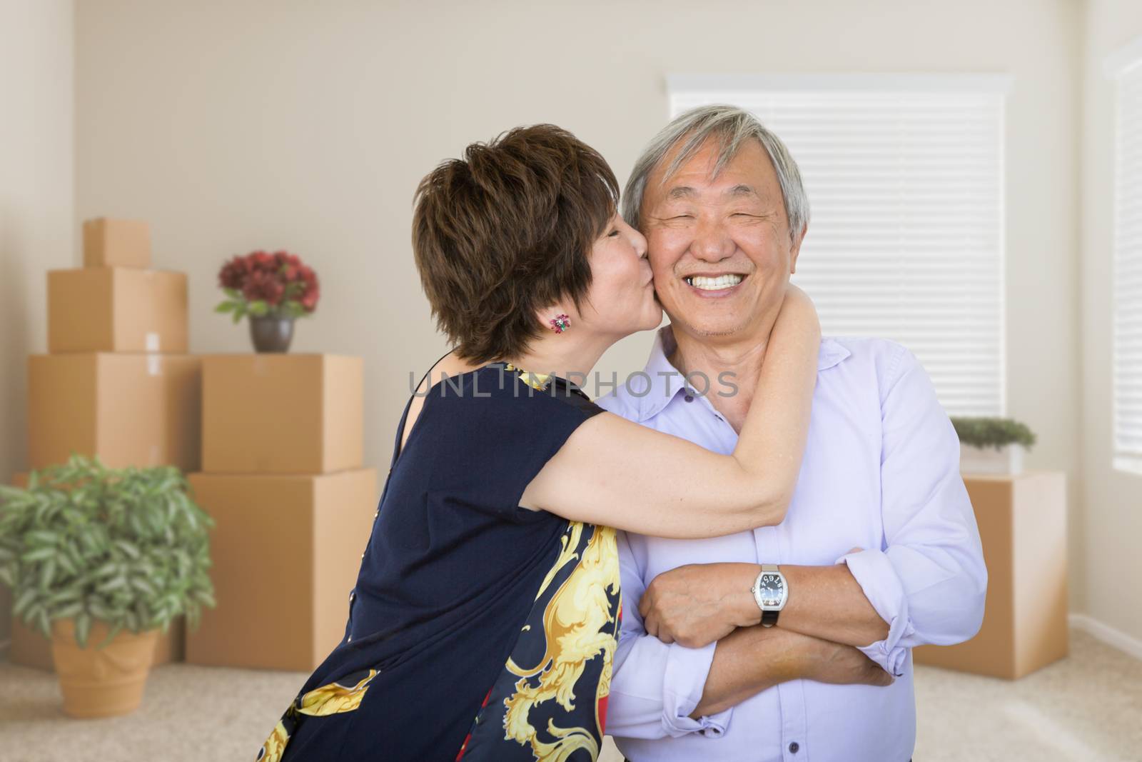 Happy Senior Chinese Couple Inside Empty Room with Moving Boxes and Plants.
