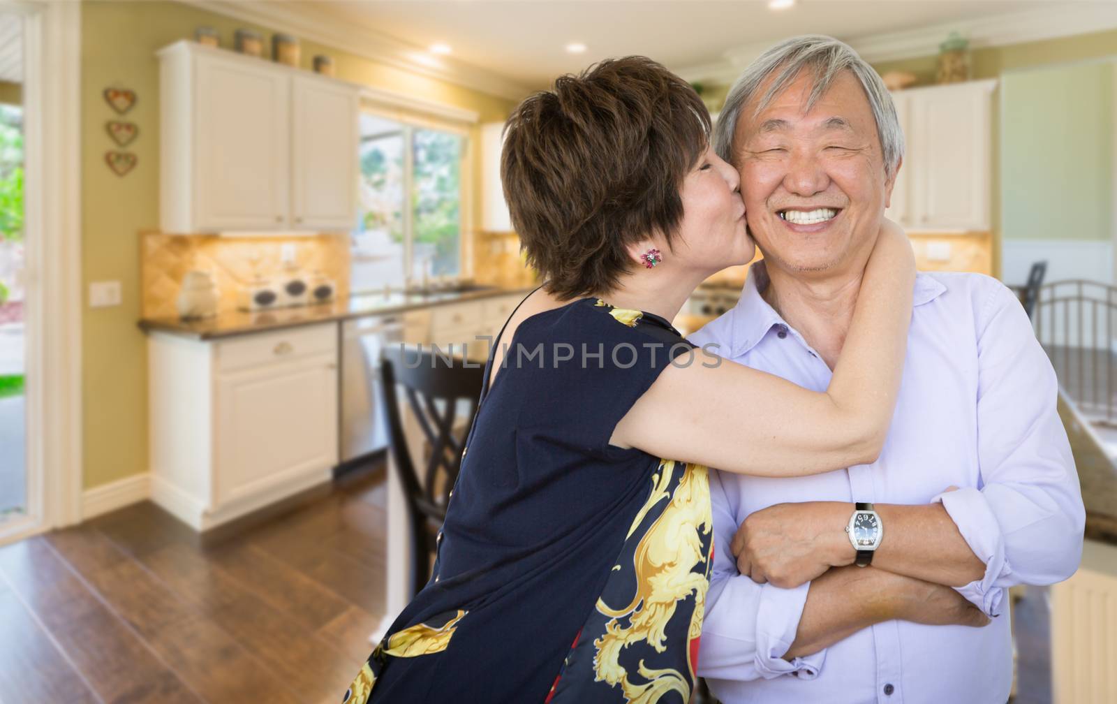 Happy Senior Chinese Couple Kissing Inside Beautiful Custom Kitchen. by Feverpitched