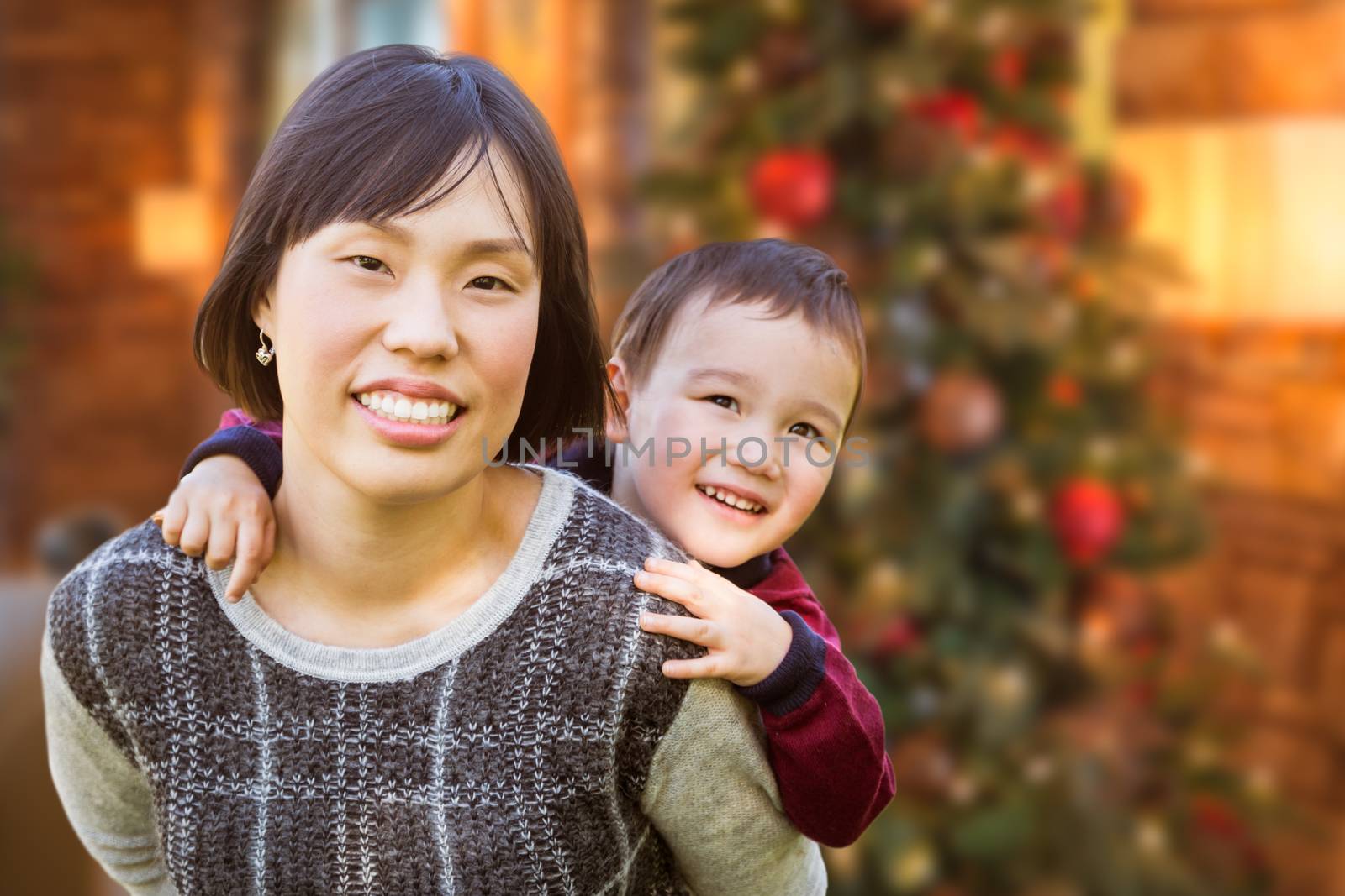 Chinese Mother and Mixed Race Child Inside House In Front of Decorated Christmas Tree.