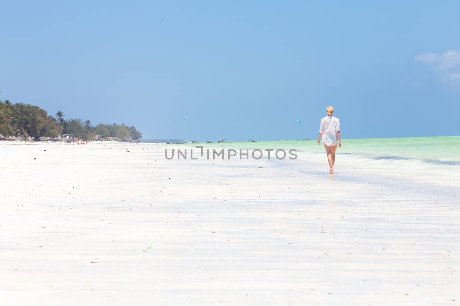 Happy woman having fun, enjoying summer, walking along white tropical beach. Beautiful caucasian model wearing white beach tunic on vacations on picture perfect Paje beach, Zanzibar, Tanzania.
