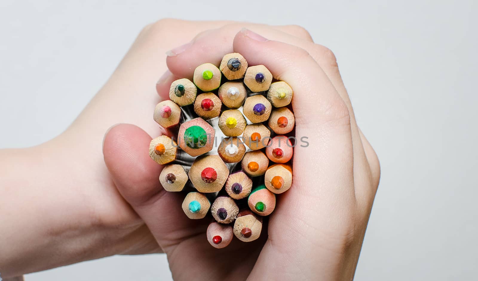 Colored pencils for painting in children's hands on a white background.