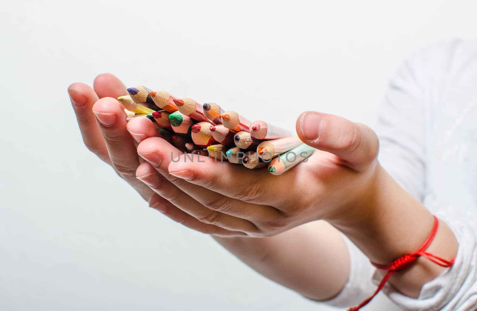 Colored pencils for painting in children's hands on a white background.