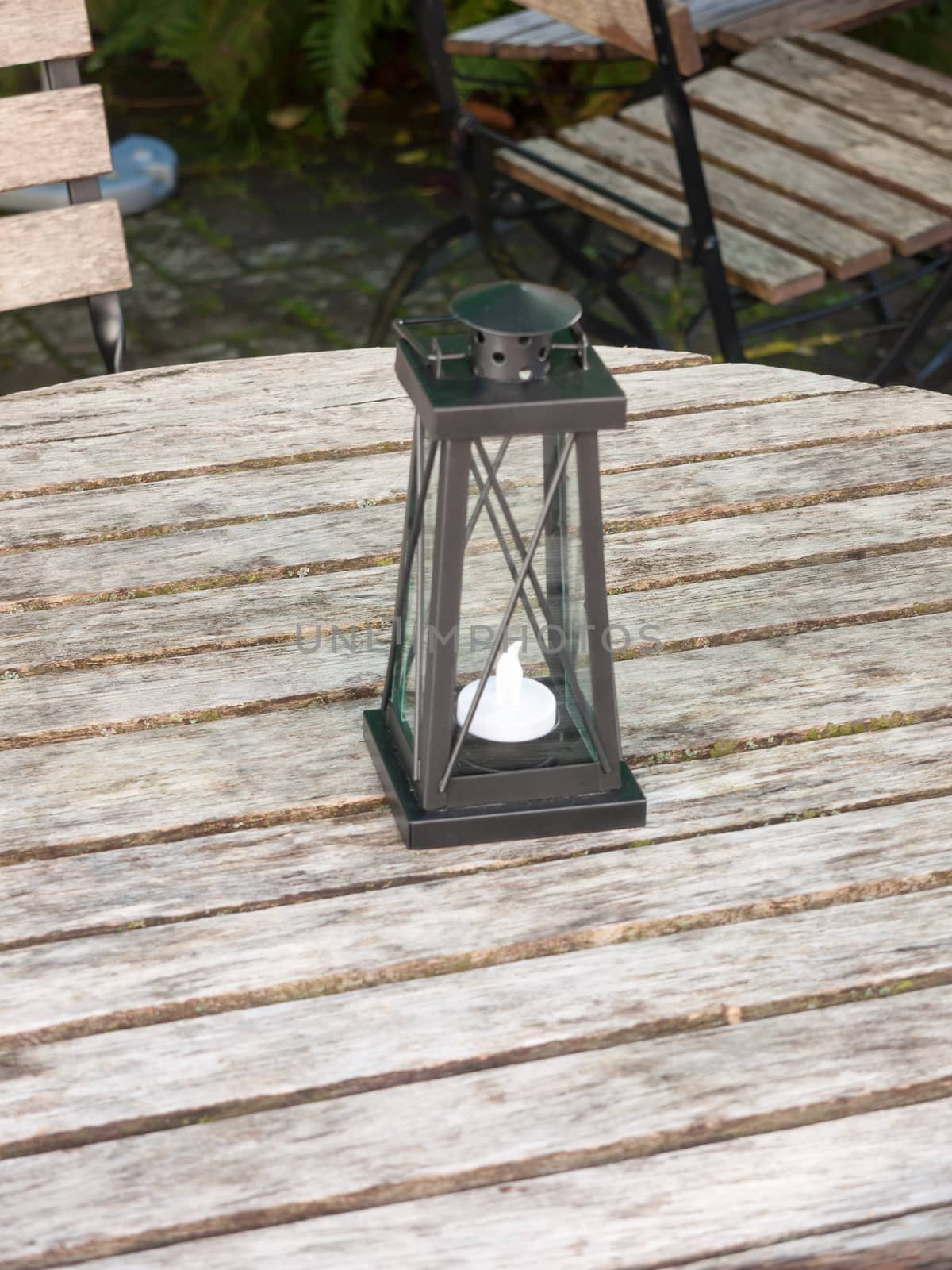 empty wooden public bench table and chairs with black lantern light box and candle ornament; essex; england; uk