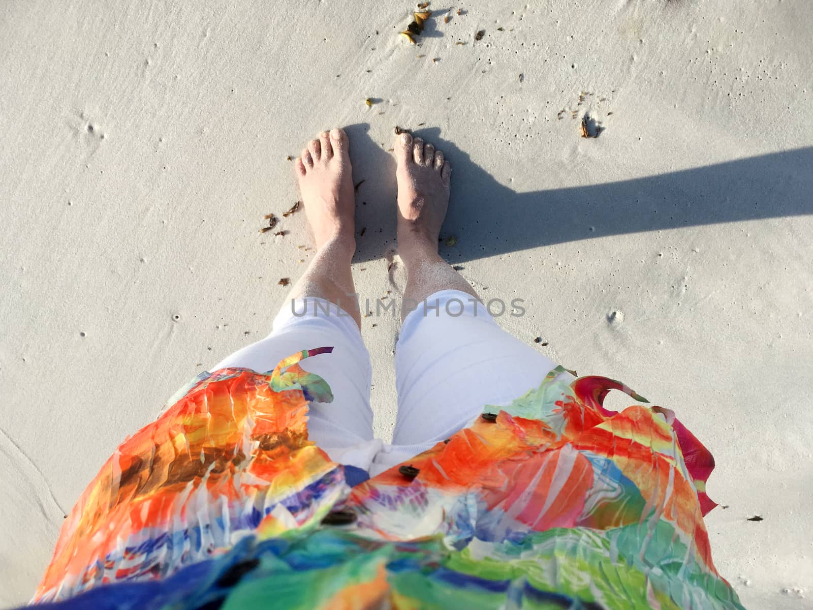 Sand covered feet and legs on the beach in early morning light with long shadows.  POV looking down