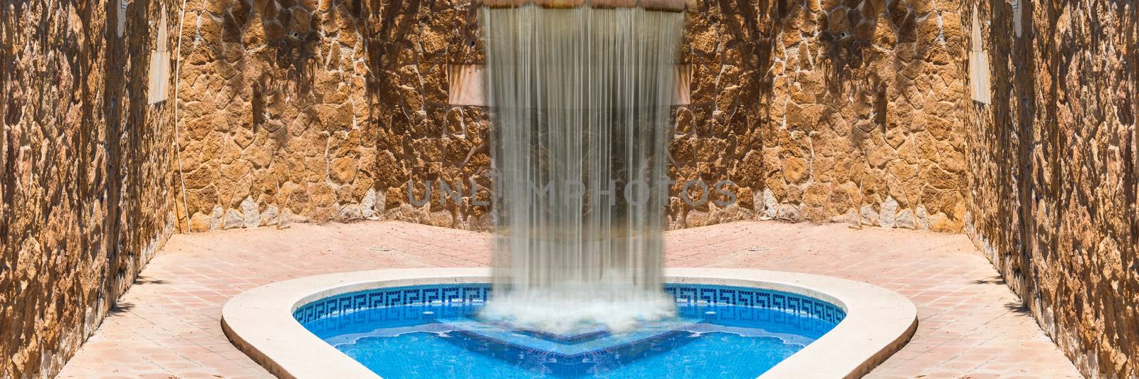 Luxury swimming pool with waterfall. In the background a mediterranean wall decorated with sandstones.