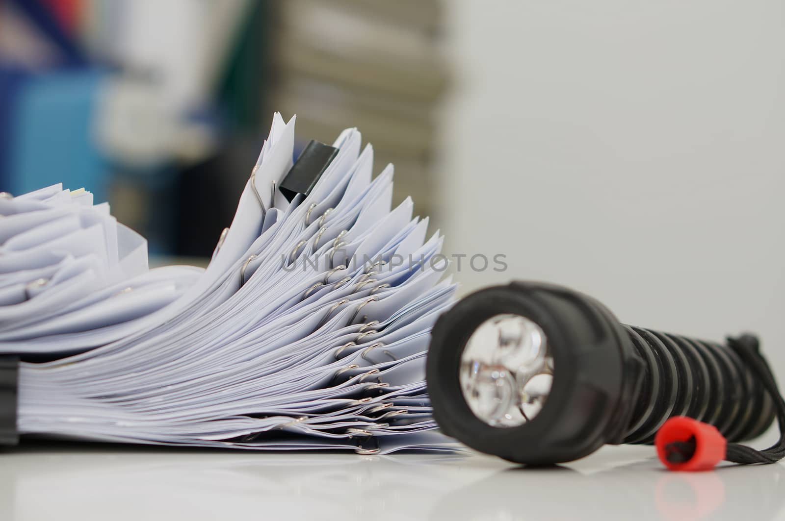 Stacks of paper files with clips on desk for report and flashlight in the office at evening by ninun