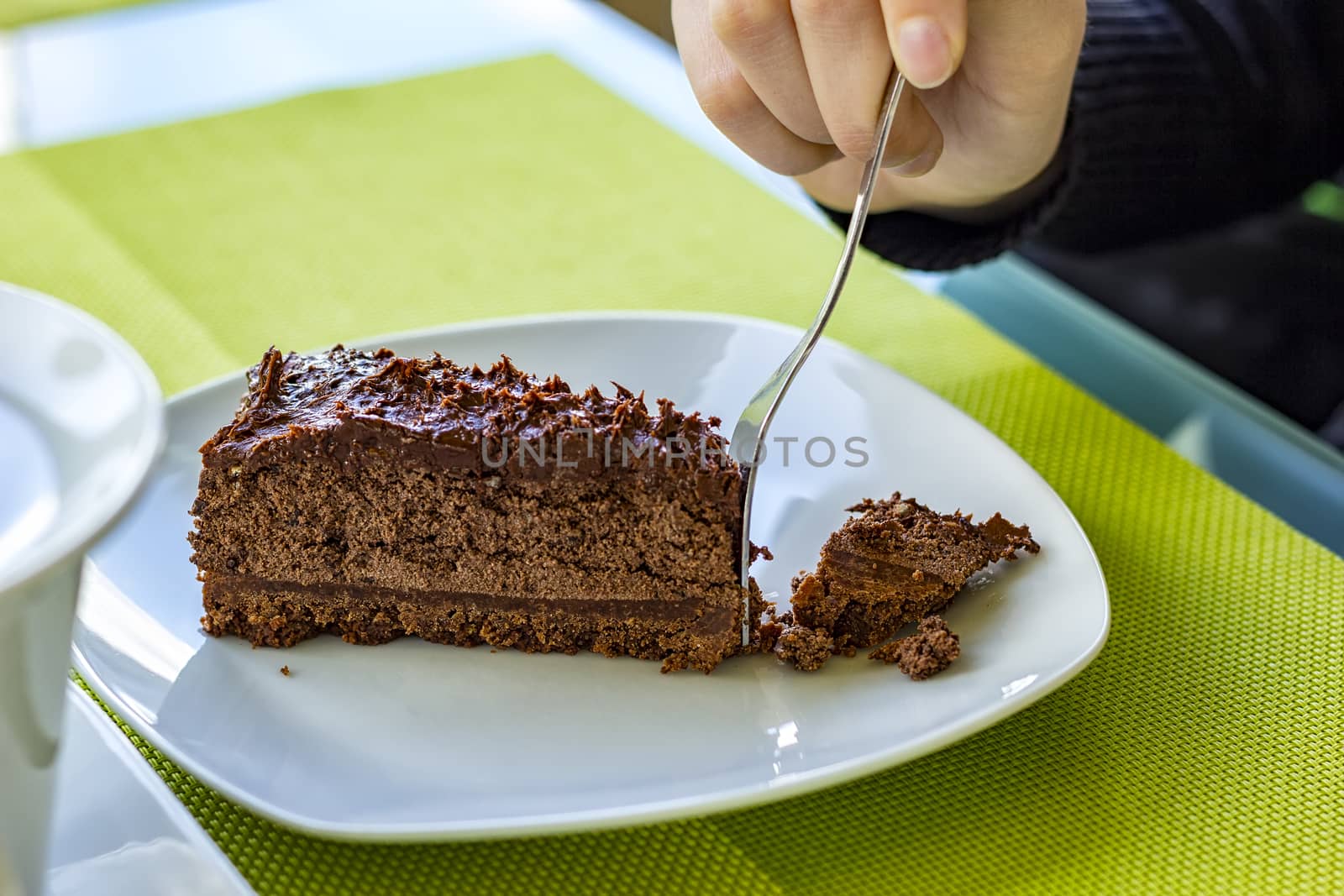A girl's hand breaks a piece of chocolate cake on a plate. Close Up
